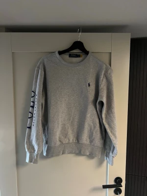 Grå sweatshirt från Polo Ralph Lauren - Klassisk grå sweatshirt från Polo Ralph Lauren med broderad marinblå logga på bröstet. 