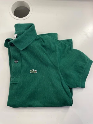 Lacoste tröja  - Jättefin grön Lacoste tröja i storlek 152cm. Passar även någon storlek större om man vill ha en tajtare passform. Använd nån gång men är i mycket bra skick!  