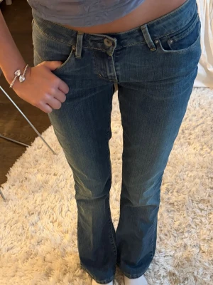 Blå bootcut jeans från Levi's - Säljer ett par klassiska blå bootcut jeans från Levi's med låg midja och fem fickor. Jeansen har en snygg tvätt och subtila slitningar, samt Levi's ikoniska läderpatch bak i midjan. Perfekta för en avslappnad och trendig look.