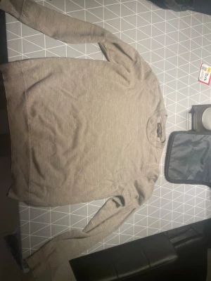 Beige rundhalsad tröja från Oscar Jacobson  - Säljer en stilren beige tröja från oscar Jacobson  med rund halsringning och långa ärmar. Tröjan har en enkel, klassisk design och är tillverkad i ett mjukt material som passar perfekt till olika outfits. Helt oanvänd 