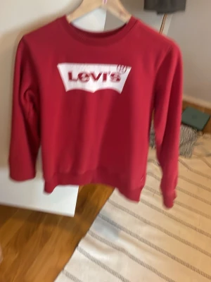 Röd sweatshirt från Levi's - Snygg röd sweatshirt från Levi's med det klassiska vita logotrycket på bröstet. Tröjan har rund halsringning och långa ärmar. Perfekt för en avslappnad och trendig stil. Tillverkad i mjukt bomullsmaterial som känns skönt mot huden.