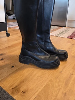 Svarta höga stövlar - Säljer ett par svarta höga stövlar med chunky sula och dragkedja på sidan. Sparsamt använda och inte defekter, säljer pga har inte fått användning för. (OBS OBS, inte de på bild 3 men väldigt likt) 