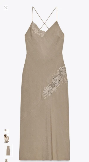 Beige omlottklänning med spetsdetaljer Zara - Snygg beige långklänning med tunna axelband som korsas i ryggen och knytning baktill. Klänningen har v-ringning och dekorativa spetsdetaljer vid bysten och på sidan. Tillverkad i ett lätt material som ger en elegant siluett.