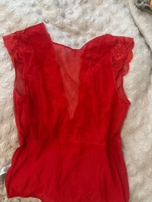 Röd spetsbody - Röd spetsbody med V-urringning. Stark röd färg och fin design som fångar ögat. 