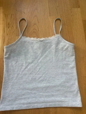 Grå linnetopp med spetsdetalj - Säljer en ljusgrå linnetopp med tunna axelband och söt spetskant upptill. Perfekt till jeans eller shorts för en chill look.