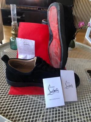 Svarta Christian Louboutin sneakers - Snygga svarta sneakers från Christian Louboutin i mocka med den ikoniska röda sulan och diskret logga undertill. Lågt skaft och klassisk snörning. Kommer med originalpåse och skötselråd. Perfekta för dig som vill ha något exklusivt och stilrent.