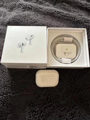 Apple AirPods Pro 2nd Gen  - Säljer ett par vita Apple AirPods Pro (2nd generation) med MagSafe-laddetui. Trådlösa in-ear hörlurar med aktiv brusreducering och transparensläge. Kommer i originalförpackning med laddkabel. Snygg och stilren design i blank plast.