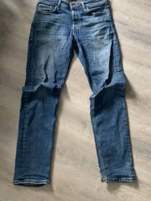 Blå raka jeans med fade - Säljer ett par klassiska blå jeans från Jack & Jones med raka ben och snygga fader framtill. Jeansen har modellen Tapered/mike med normal midja och stängs med dragkedja och knapp. Perfekta för en avslappnad och trendig stil