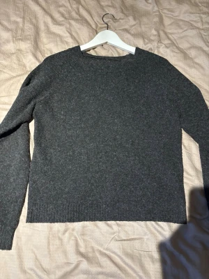 Mörkgrå stickad tröja - En enkel och stilren mörkgrå stickad tröja med rund halsringning och långa ärmar. Tröjan har ribbstickade muddar vid ärmslut och nederkant. Perfekt för lager-på-lager och passar till det mesta.