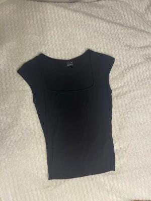 Svart topp från Gina - En stilren svart topp från Gina Tricot med fyrkantig ringning och ärmlös design. Toppen har en slim passform och är tillverkad i ett mjukt, stretchigt material som sitter snyggt på kroppen. Perfekt att matcha med jeans eller kjol. Knappast använt