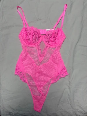 Rosa spetsbody - Superfin neonrosa spetsbody från Nelly i modellen ”UW Endless love body”. Den har en fantastisk färg, bygelkupor för bra stöd och justerbara axelband samt knäppning i ryggen för perfekt passform. Bodyn har hel gren (inget knäppe) och är i thong-modell baktill. Den är i nyskick då den bara är använd 2 gånger och modellen är helt slutsåld i butik. Storlek XS. Kolla gärna min profil för liknande annonser! Jag erbjuder bundle-rabatt vid köp av flera produkter.