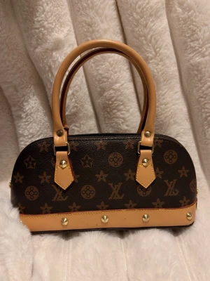 Vintage handväska - Snygg handväska från. Väskan har guldfärgade nitar och dragkedja upptill.