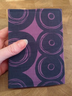 Lila anteckningsbok med grafiskt mönster - Unik anteckningsbok i tyg med mörklila och lila grafiskt cirkelmönster. Anteckningsboken har en mjuk och flexibel känsla, perfekt för dig som gillar färg och mönster. Storlek A6 med ca 100 blanka sidor