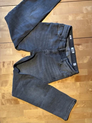 Grå raka jeans från Jack & Jones - Säljer ett par grå jeans från Jack & Jones med rak passform och klassisk femficksdesign. Jeansen har normal midja och är tillverkade i stretchigt denimtyg för extra komfort. Perfekta för en avslappnad och stilren look.