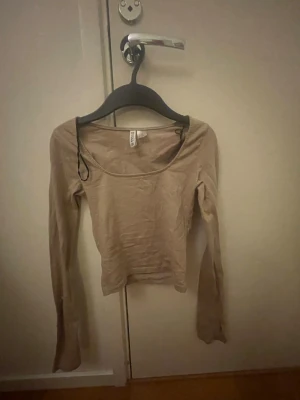 Beige croppad långärmad topp - Trendig beige croppad topp från h&m med lång ärm och rundad urringning. Sitter tight och är perfekt att styla med höga jeans eller kjol. Enkel och stilren design som passar till många olika looks.