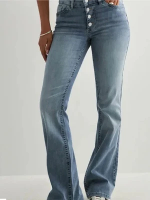Bootcut jeans - Snygga ljusblå bootcut jeans med knappar framtill. Jeansen har klassiska bakfickor och är tillverkade i stretchigt denimtyg för en bekväm passform. Perfekta för en trendig och avslappnad look.