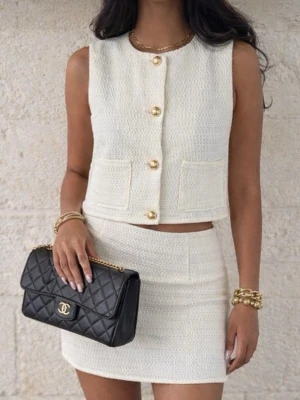 Vit ärmlös set med knappar - Stilren vit väst samt kjol i strukturerat tyg med guldfärgade knappar framtill och två fickor. Västen är ärmlös och har en rak, figurnära passform som ger en chic look. Perfekt för dig som gillar minimalistisk och elegant stil.