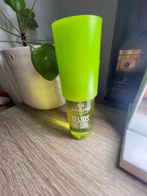 Sol de Janeiro Beijos de Sol parfym - Fräsch parfym från Sol de Janeiro med namnet Beijos de Sol. Flaskan är transparent med en stor, limegrön kork och text i vitt. Doften ger tropiska vibbar och flaskan har en modern, ungdomlig design som sticker ut på hyllan.