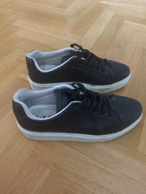 Svarta sneakers med vit sula  - Stilrena svarta sneakers från NA-KD med klassisk låg profil och tjock vit sula. Skorna har svarta skosnören och en enkel, clean design. Insidan är fodrad i vitt tyg och ovandelen är i slätt läderliknande material.