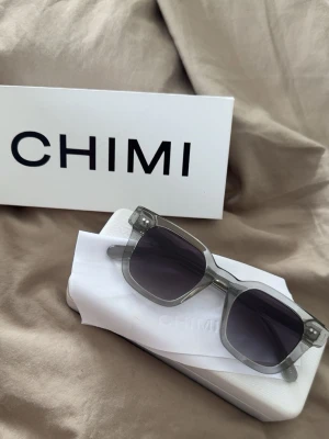 CHIMI 04 - Solglasögon från CHIMI med transparent grå båge och mörka fyrkantiga glas, modellen 04. Kommer med originalfodral, putsduk samt box. Perfekta till sommaren!!