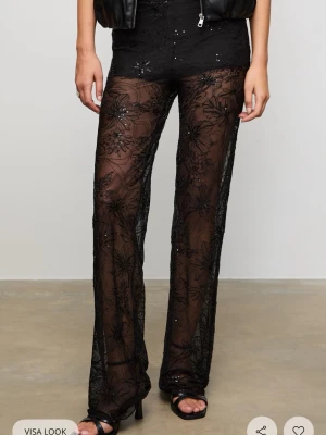 Svarta mesh-leggings med blommor - Säljer ett par svarta mesh-leggings med transparent material och broderade blommor samt paljettdetaljer. De har utsvängda ben och hög midja för en trendig look. Perfekta för dig som vill sticka ut och addera lite edge till outfiten., slutsålda 