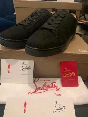 Svarta sneakers från Christian Louboutin - Snygga svarta sneakers från Christian Louboutin i mocka med klassisk röd sula och diskret logga. Skorna har svarta skosnören, låg profil och stilren design som passar till det mesta. Kommer med originalkartong och dustbag.