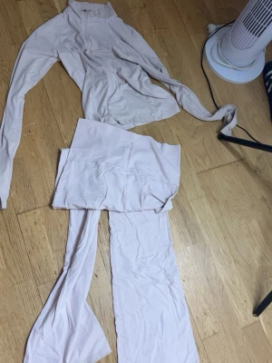 Ljusrosa loungewear set med zip - Mysigt loungewear set i ljusrosa med långärmad ziptröja och matchande byxor med utsvängda ben. Tröjan har dragkedja framtill och hög krage. Perfekt för chill dagar hemma eller när du vill vara bekväm men ändå snygg.