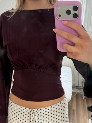Mörkröd långärmad topp - Snygg mörkröd croppad topp med långa ärmar och figurnära passform. Toppen har en markerad söm under bysten som ger en cool detalj. Perfekt att styla med höga jeans eller kjol. Prislappen är kvar
