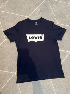 Mörkblå Levi's t-shirt med logga - Snygg mörkblå t-shirt från Levi's med klassisk vit logga framtill. T-shirten har rund halsringning och korta ärmar. Tillverkad i mjuk bomull för skön känsla och passar perfekt till jeans eller shorts.