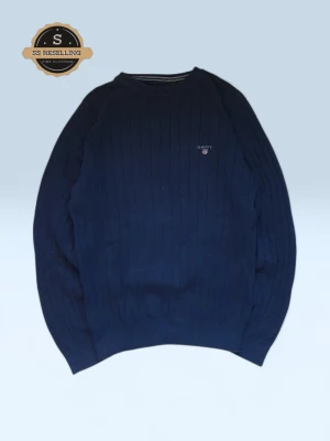 Mörkblå stickad tröja från GANT - Mörkblå stickad tröja från GANT med diskret logga broderad på bröstet. Tröjan har rund halsringning och ribbade muddar vid ärmslut och nederkant. Klassisk rak passform och vertikalt ribbstickat mönster för en stilren look.