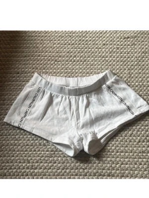 Vita trosor från Calvin Klein - Snygga vita trosor från Calvin Klein med logotyp längs sidorna. De har en boxermodell och är tillverkade i mjukt och stretchigt material som ger en bekväm passform. Perfekta för dig som gillar klassisk och stilren design.