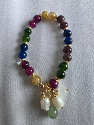Armband  - Unikt armband med stora runda pärlor i flera färger som blått, grönt, gult, lila och vinrött. Armbandet har guldfärgade detaljer och tre dekorativa hängen med vita oregelbundna pärlor och stenar. Perfekt för dig som gillar färg och statement-accessoarer.