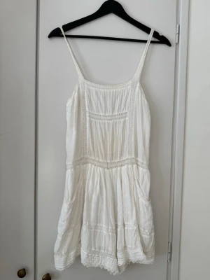 Vit somrig kortklänning shorts med spets Maje - Söt vit kortklänning / shorts klänning med tunna axelband och fina spetsdetaljer. Klänningen har en luftig passform och är tillverkad i ett lätt material, perfekt för varma dagar. Dekorativa sömmar och volangkant nedtill ger en romantisk känsla.strl är märkt en 38:a men skulle säga den är mer passande till en strl 36
