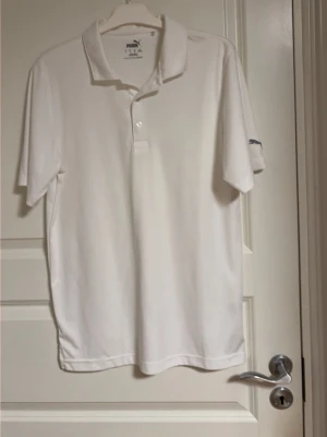 Vit pikétröja från Puma - Klassisk vit pikétröja från Puma med korta ärmar och krage. Tröjan har två knappar vid halsen och Puma-logga på ärmen. Tillverkad i ett lätt och bekvämt material som passar perfekt till sport eller golf.