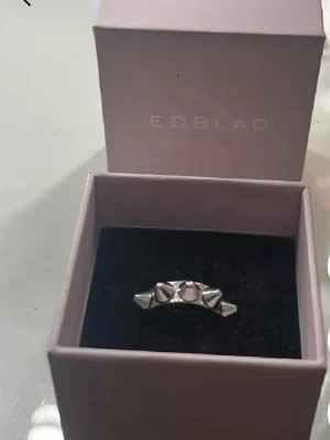 Silvrig ring med nitar från Edblad - Säljer en cool silvrig ring från Edblad med markerade nitar runt hela ringen. Ringen har en modern och edgy design i metall och kommer i originalask. Perfekt för dig som gillar statement-smycken.