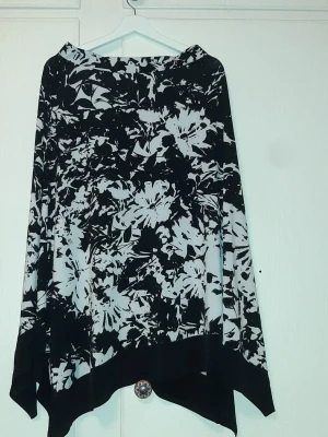 Svartvit blommig långkjol från Bonmarché  - Säljer en svartvit långkjol med blommigt mönster och asymmetrisk nederkant. Kjolen har bred midja och är tillverkad i ett mjukt, följsamt material som ger ett snyggt fall. Perfekt för dig som gillar statement-plagg med unik design.