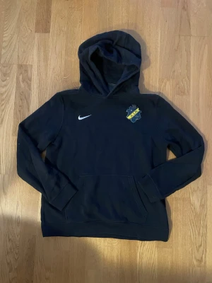 Svart AIK hoodie från Nike - Svart hoodie i storlek 158-170 cm från Nike med AIK:s klubbmärke tryckt på bröstet. Klassisk huva och känguruficka framtill. Perfekt för dig som vill representera ditt favoritlag på ett stilrent sätt. Tillverkad i mjukt material för skön känsla.
