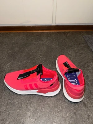 Rosa slip-on sneakers från Adidas - Snygga rosa slip-on sneakers från Adidas med vita sulor och svarta detaljer på ovansidan. Skorna har en modern design utan snörning och är tillverkade i ett lätt och ventilerande material. Perfekta för dig som vill ha en sportig och trendig look.