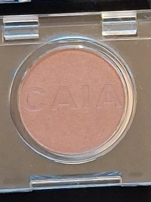 CAIA champange färgad ögonskugga - Säljer en rund, skimrande champagne färgad ögonskugga från CAIA i en genomskinlig plastförpackning. Skuggan har en mjuk, skimrande finish och är enkel att applicera för en fräsch look. Perfekt för dig som gillar varma toner och vill ha en smidig singelskugga i sminkväskan.