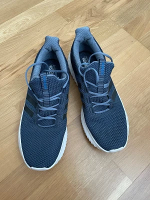 Mörkblå Adidas sneakers med vita sulor - Snygga mörkblå sneakers från Adidas med stickad ovandel och klassiska svarta ränder på sidorna. Skorna har vita, räfflade sulor med cloudfoam-dämpning och matchande blå skosnören. Perfekta för en sportig och avslappnad stil.
