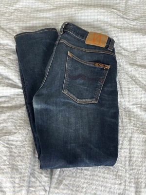 Lean dean jeans från Nudie Jeans 30/32 - Snygga mörkblå jeans från Nudie Jeans med klassisk femficksmodell och kontrastsömmar. Jeansen har en rak passform och är tillverkade i slitstark denim med en cool tvättad look. Perfekta för dig som gillar stilrena och tidlösa jeans.