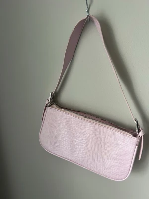 Ljusrosa axelväska Gina Tricot - Snygg ljusrosa axelväska från Gina Tricot i fejkläder med croco-mönster. Väskan har en bred axelrem och dragkedja upptill. Perfekt storlek för det viktigaste och ger en trendig touch till din outfit. Väskan är i nästan nyskick och använd endast ett fåtal gånger! bara att skriva vid frågor eller funderingar 🥰 Priset kan diskuteras! 