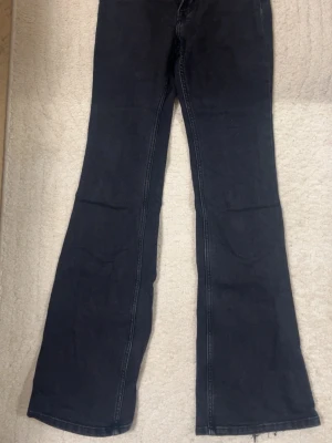 Mörkgråa/Svarta högmidjade bootcut jeans - Säljer ett par svarta bootcut jeans med rå kant nertill. Jeansen har hög midja, klassiska bakfickor och markerade sömmar längs benen. Perfekta för dig som gillar en retro och avslappnad stil.