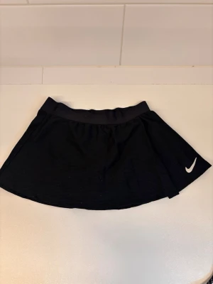 Tenniskjol från Nike - Tenniskjol från Nike för barn. Lite smutsigt därav priset, går bort i tvätten. Storlek 128/137.
