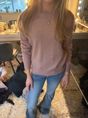 Ljusrosa stickad tröja - Mysig ljusrosa stickad tröja med rund halsringning och ribbade muddar vid ärmslut och nederkant. Enkel och stilren design som passar perfekt till jeans eller kjol. Tröjan har en avslappnad passform och är tillverkad i ett mjukt material.
