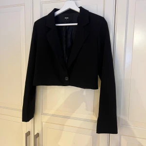 Svart cropped kavaj från BikBok - Stilren svart cropped / kort kavaj från BikBok. Endast använd 1 gång. 