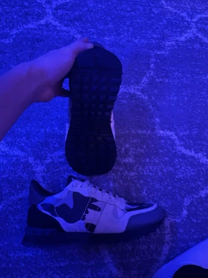 Valentino Rockrunner - Snygga sneakers från Valentino med coolt camo-mönster i svart, grått och vitt. Skorna har klassisk snörning, robust gummisula och detaljer i läder och textil. Perfekt för dig som vill sticka ut med stilrena och trendiga skor. Ställ gärna frågor
