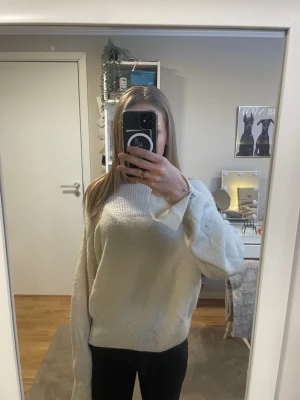 Beige stickad tröja med pärldetaljer - Mysig stickad tröja i beige med bred ribbad halsringning och långa ärmar. Ärmsluten har fina pärldetaljer som ger en extra touch. Perfekt för att hålla sig varm och snygg under kyliga dagar.