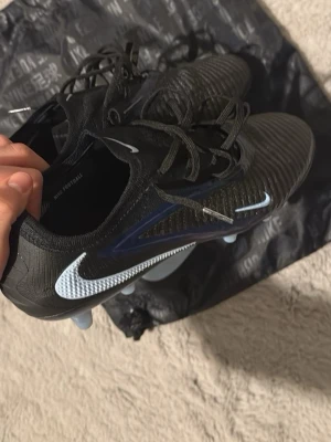 Nike Mercurial svart/blå fotbollsskor - Snygga Nike Mercurial fotbollsskor i svart med blå och vita detaljer. HELT OANVÄNDA! Min lillebror köpte fel storlek och glömde skicka tillbaka skorna och nu säljer jag skorna åt honom. Skriv privat för mer frågor och pris!