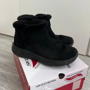 Vinterskor från Skechers Arch Fit - Säljer ett par svarta boots från Skechers Arch Fit med mjuk och fluffig fuskpäls inuti. Skorna har en robust sula och är tillverkade i mockaliknande material. Perfekta för kyliga dagar när du vill ha både stil och komfort.  (OBS!! rengör dem så gott det går så bortse från smuts på sulan)